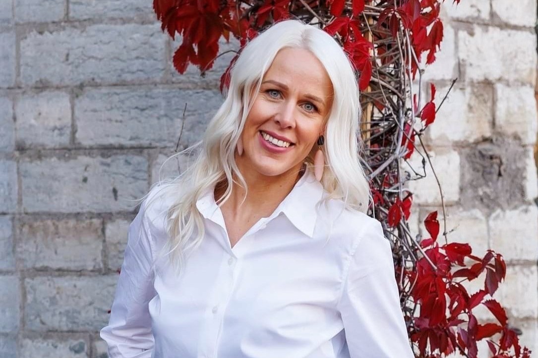 Loodusmuuseumi inimeste ja töökultuuri juht Kairit Kalvik seismas paekiviseina ees, selja taga punaste lehtedega viinamarjaväädid