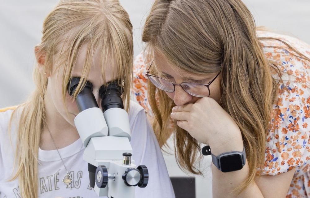 Blondi peaga tüdruk vaatamas mikroskoopi, temast paremal õpetaja